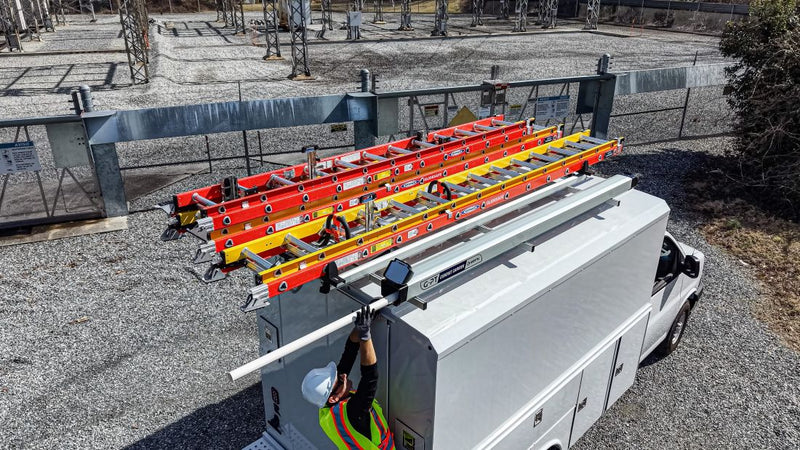 conduit carrier on van roof rack with orange ladders on drop down ladder rack and a man pulling out pipe out of the conduit carrier